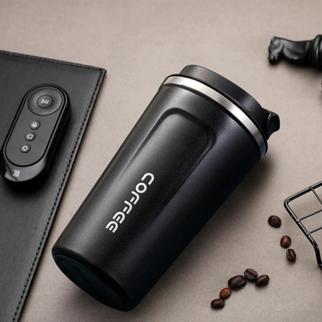 Black stainless steel vacuum insulated coffee travel mug with leakproof lid placed on a modern office desk.