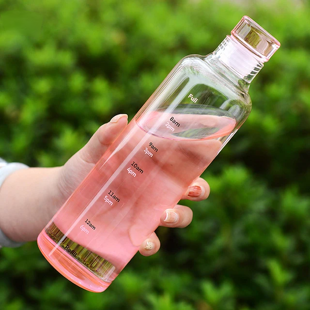 Hand holding pink glass water bottle with time marker outdoors